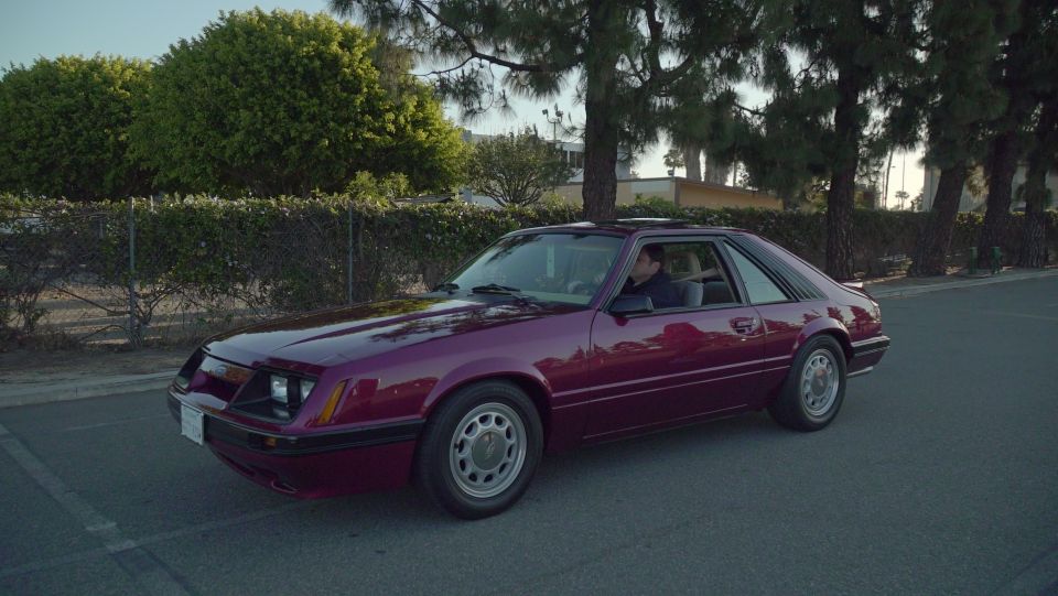 Maroon sedan parked on the side of the road, trees in background