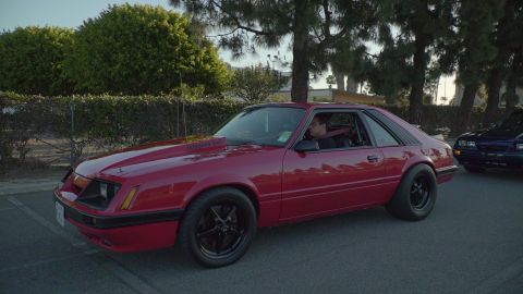 1993 Ford Taurus - Red Ford Mustang hatchback with hood scoop and black wheels seen driving alongside another vehicle.
