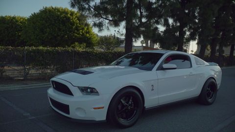 1993 Ford Taurus - A white Ford Mustang with racing wheels and a hood scoop is parked outdoors.