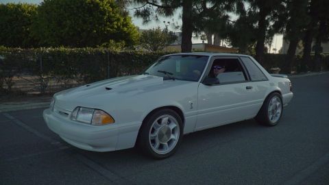 1993 Ford Taurus - A white 1993 Ford Mustang coupe is shown from a three-quarter front view, hood scoops and distinctive wheels.
