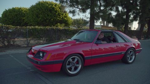 1993 Ford Taurus - Red 1985 Ford Mustang hatchback with a driver visible inside.