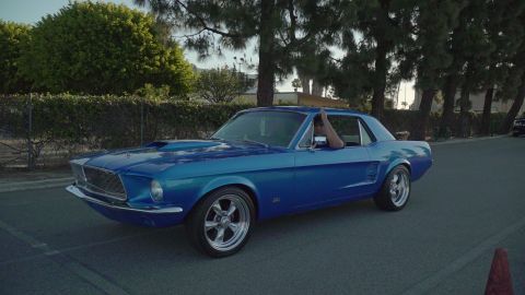 1993 Ford Taurus - A blue 1967 Ford Mustang coupe cruises down the road, its driver's arm resting on the open window.
