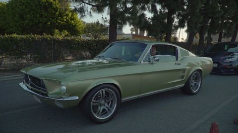 1993 Ford Taurus - A green 1967 Ford Mustang fastback is parked on the street with another vehicle behind it.