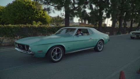 1993 Ford Taurus - A teal 1971 Ford Mustang coupe is seen driving on a road with trees and a hedge in the background.