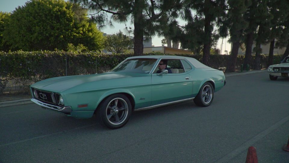 1971 Ford Mustang coupe driving on a street, another car visible in the background