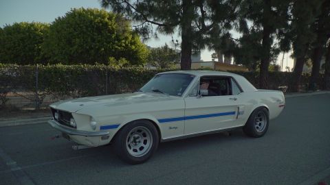 1993 Ford Taurus - A classic white Ford Mustang with blue side stripes is parked outdoors on a paved surface.