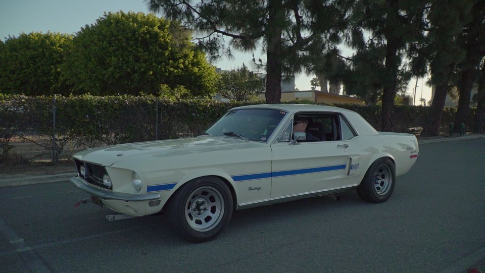 White 1967 Ford Mustang with blue racing stripes parked on asphalt