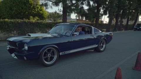 1993 Ford Taurus - A dark blue 1966 Ford Mustang fastback, identified by its "GT 350" badging and classic body style, cruises down a street.