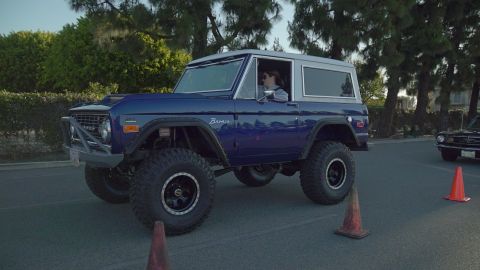 1993 Ford Taurus - A lifted blue 1975 Ford Bronco with off-road tires is seen from the side, with another classic car in the background.