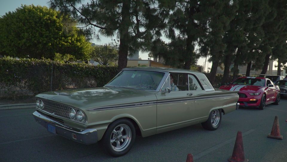 Old gold coupe with chrome trim driving, red modern car behind it