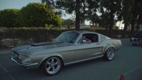 1993 Ford Taurus - A silver 1967 Ford Mustang Fastback drives past a black classic car.