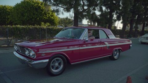 1993 Ford Taurus - A red 1963 Ford Falcon Sprint coupe is seen driving on a street with trees and a fence in the background.