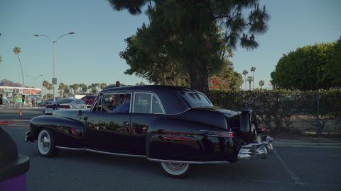 1993 Ford Taurus - A classic black sedan with a continental kit drives past other vehicles on a sunny day.
