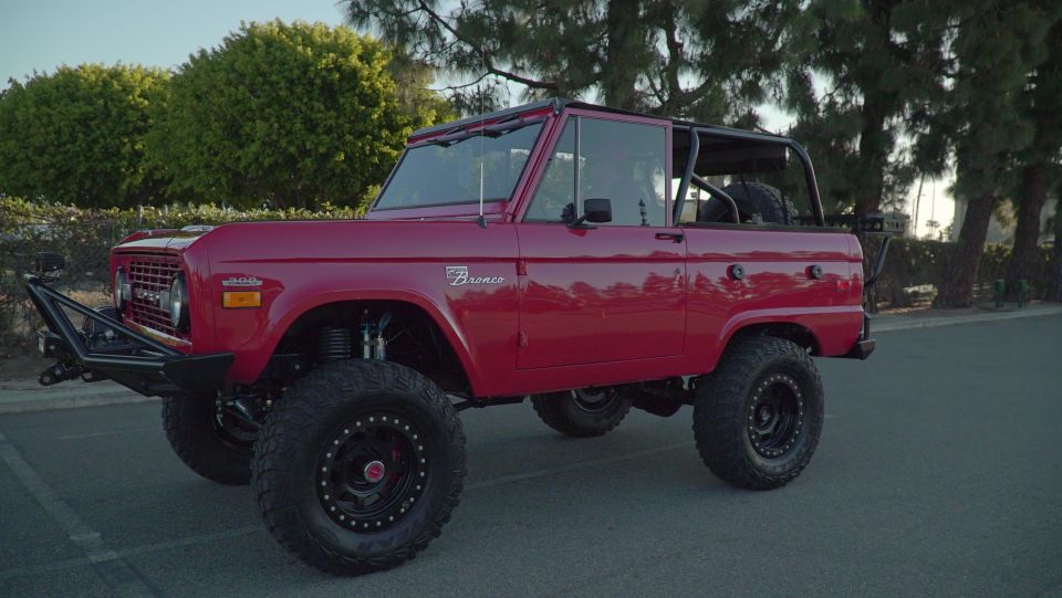 Red 1975 Ford Bronco with off-road tires and a roll cage