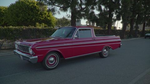 1993 Ford Taurus - A red pickup truck is parked on a street with trees and a hedge in the background.