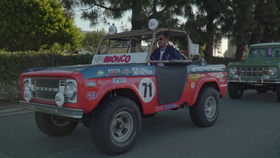 Red Ford Bronco with racing decals and a driver, green Ford Bronco behind it