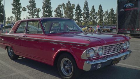 1993 Ford Taurus - A classic red Ford Starliner is displayed at an outdoor car event, with other vehicles and a Ford trailer visible.