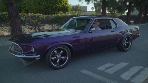 1993 Ford Taurus - A purple 1969 Ford Mustang coupe is driven on a street.