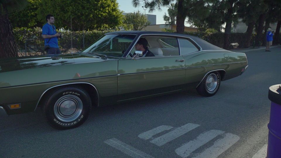 Green 1969 Ford Galaxie driving on pavement, driver visible inside