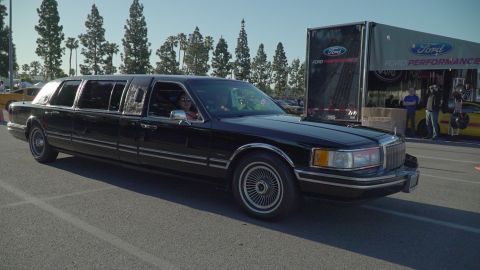 1993 Ford Taurus - A black limousine is parked near a Ford Performance trailer at an event.