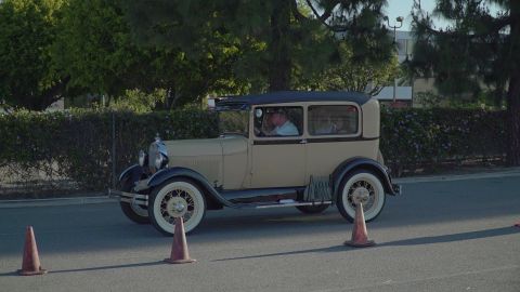 1993 Ford Taurus - A 1928 Ford Model A sedan is seen from the side, with people inside, driving past traffic cones.