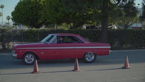 1993 Ford Taurus - A red 1963 Ford Falcon coupe drives past traffic cones on a sunny day.