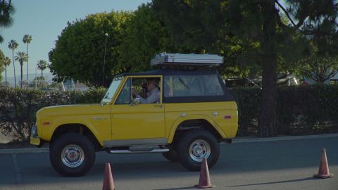 1993 Ford Taurus - A yellow 1975 Ford Bronco is driven on a paved surface, equipped with a roof rack and a black soft top.