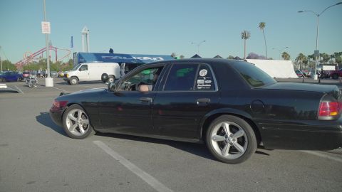 1993 Ford Taurus - A black sedan, possibly a 2000 Ford Crown Victoria, is parked in a lot with other vehicles and amusement park rides in the background.
