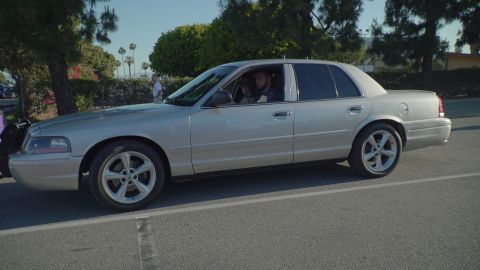 1993 Ford Taurus - This silver sedan, likely a Ford Crown Victoria, is seen from the side with tinted windows and aftermarket wheels.