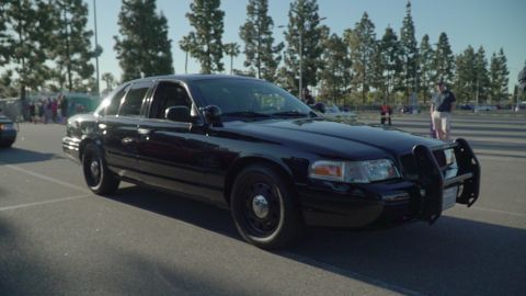 1993 Ford Taurus - A black police car with a push bar is seen from the front-right at a car show.