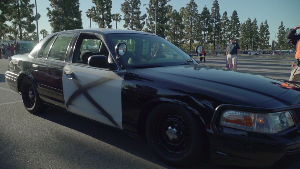 Black and white police car with large X spray-painted on the side door