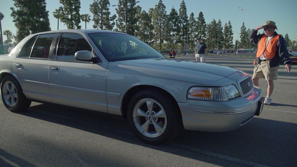 Silver Ford Crown Victoria with a man in an orange vest standing next to it