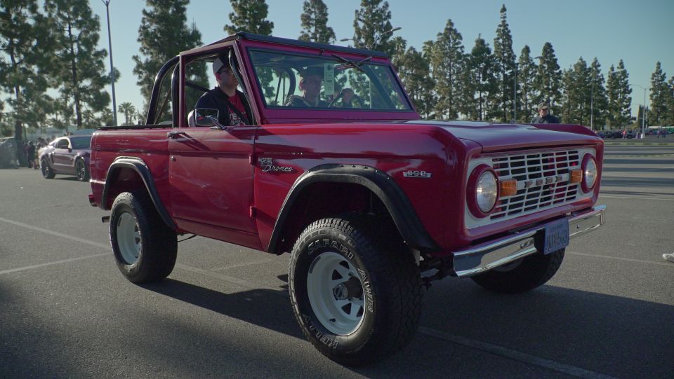 Red first-generation Ford Bronco with white wheels and chrome grille