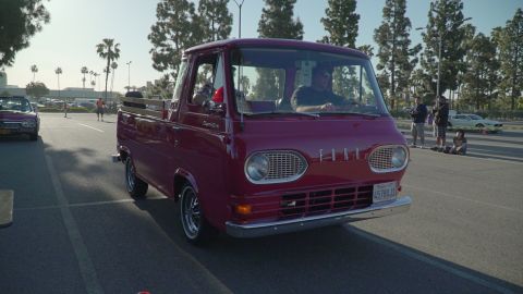 1993 Ford Taurus - Red 1961 Ford Econoline pickup truck with chrome grille and bumper, driving on asphalt.