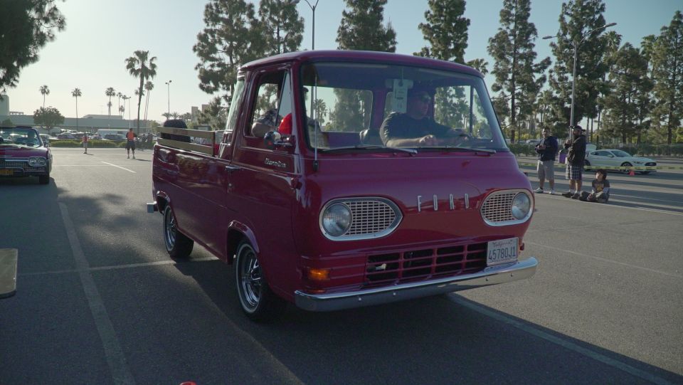 Red 1961 Ford Econoline pickup truck with chrome grille and bumper, driving on asphalt