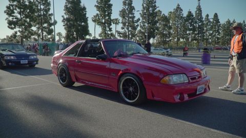 1993 Ford Taurus - A red Ford Mustang is parked at an outdoor car show, with another Mustang visible in the background.