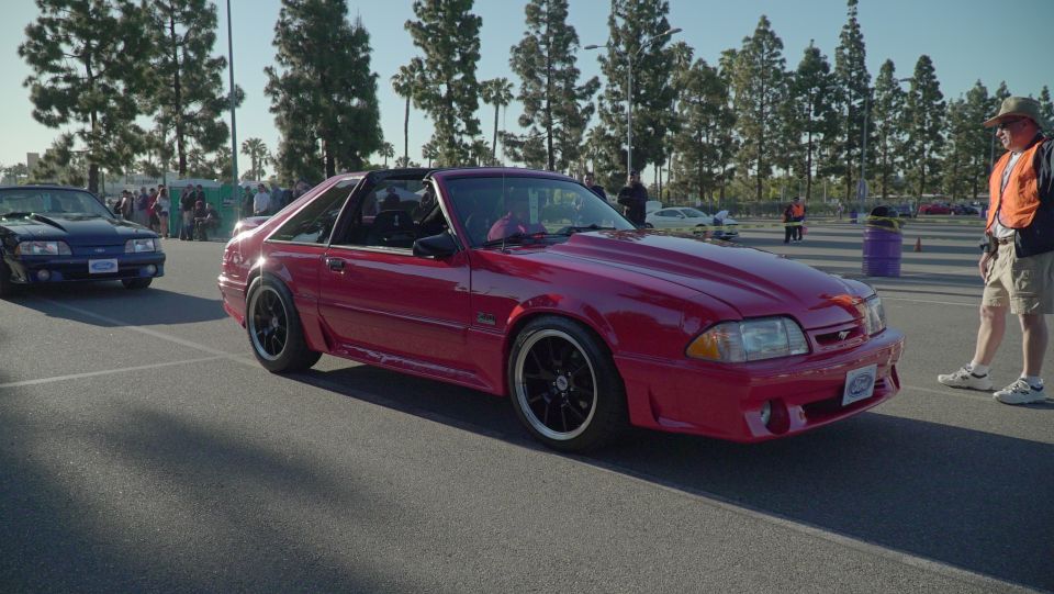 Red 1993 Ford Mustang with black wheels, parked next to a blue Mustang