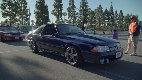 1993 Ford Taurus - A dark blue Ford Mustang is parked on asphalt with a man in an orange vest standing nearby.