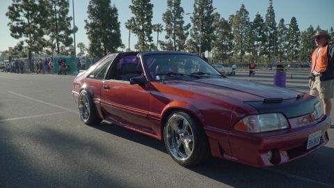 1993 Ford Taurus - A red 1993 Ford Mustang coupe is displayed at an outdoor car show, custom wheels and a car bra.