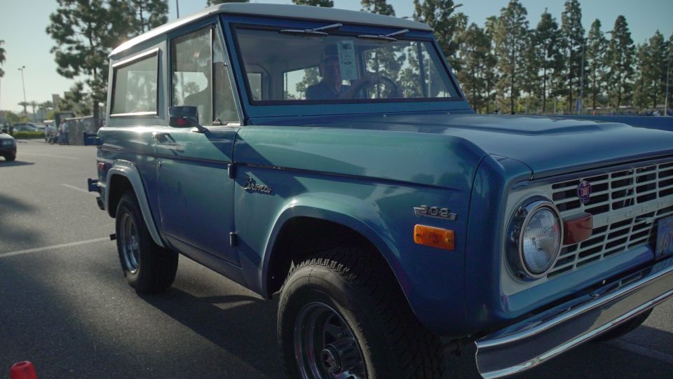 Blue first-generation Ford Bronco with white roof, parked outdoors