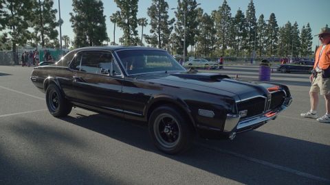 1993 Ford Taurus - A black 1969 Mercury Cougar XR7 coupe is parked at an outdoor car show, a prominent hood scoop and distinctive orange grille accents.