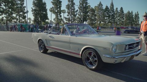1993 Ford Taurus - A 1965 Ford Mustang convertible is parked at an outdoor event with people in the background.