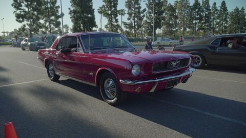 1993 Ford Taurus - A red 1965 Ford Mustang coupe is seen from the front quarter angle, with another classic car to its right.