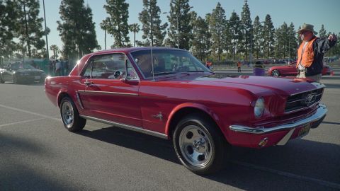 1993 Ford Taurus - A bright red 1965 Ford Mustang coupe is parked at an outdoor car show, with other vehicles and spectators in the background.