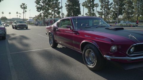 1993 Ford Taurus - Maroon 1969 Ford Mustang Mach 1 parked at an outdoor car show with other vehicles visible.