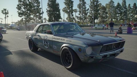 1993 Ford Taurus - A vintage Ford Mustang, modified for racing, sits on a paved surface with trees and spectators in the background.
