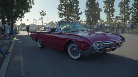 1993 Ford Taurus - A classic red convertible cruises down the street at a car show.