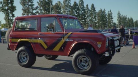 1993 Ford Taurus - A red 1975 Ford Bronco with distinctive racing stripes is parked outdoors at a car show.