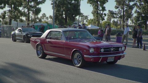 1993 Ford Taurus - A classic red 1965 Ford Mustang coupe is seen at a Ford car show, with a modern black car in the background.