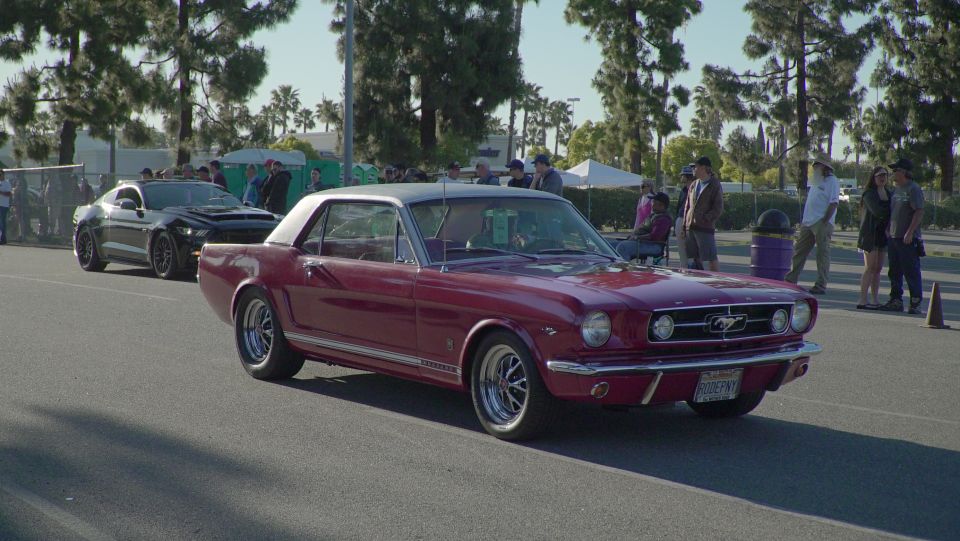 Red 1965 Ford Mustang coupe with a black roof, driving past a black modern car